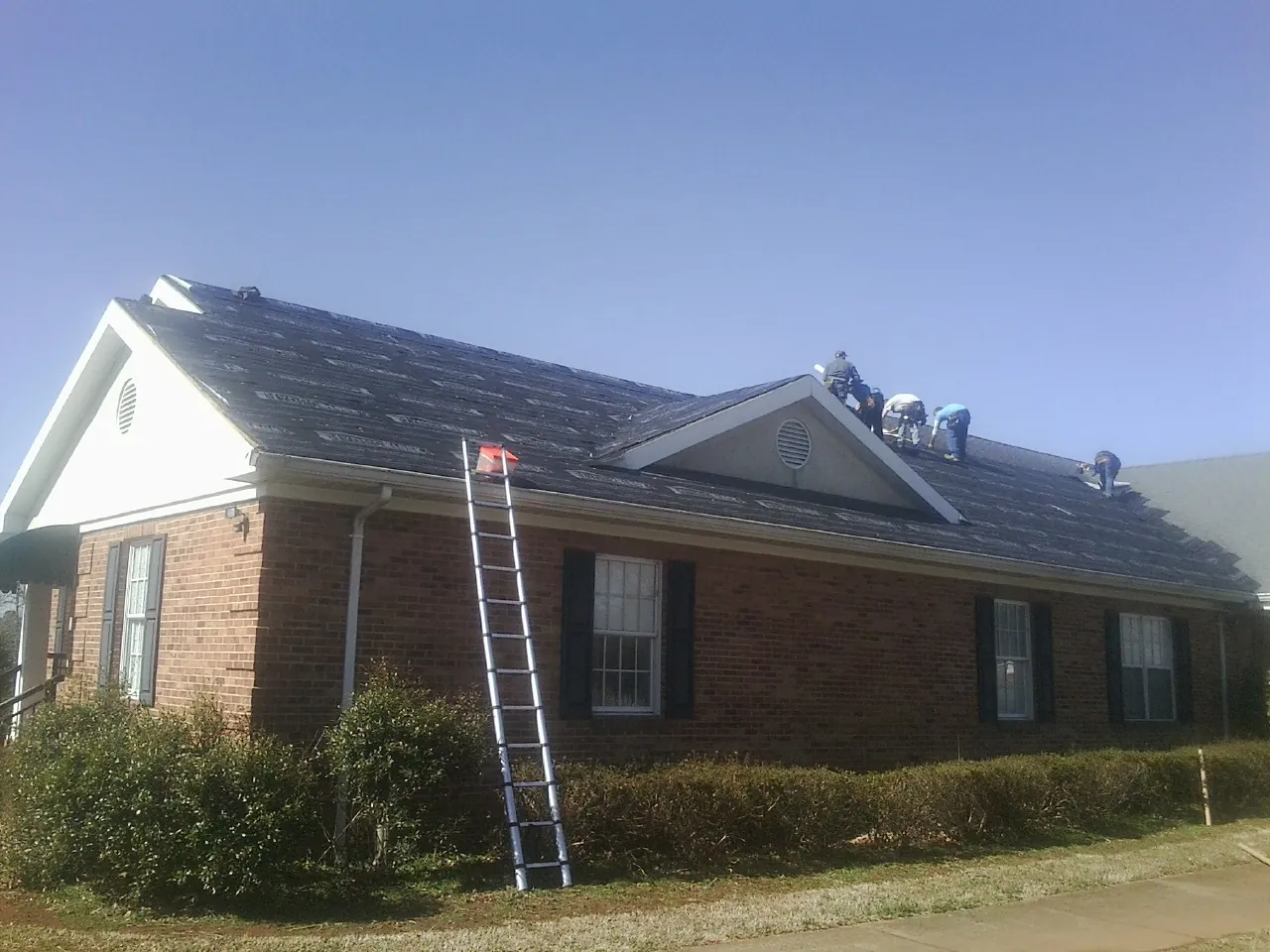 Crew tearing shingles off a brick ranch roof with a ladder set — Emergency Roof Repair work by our crew in Deridder
