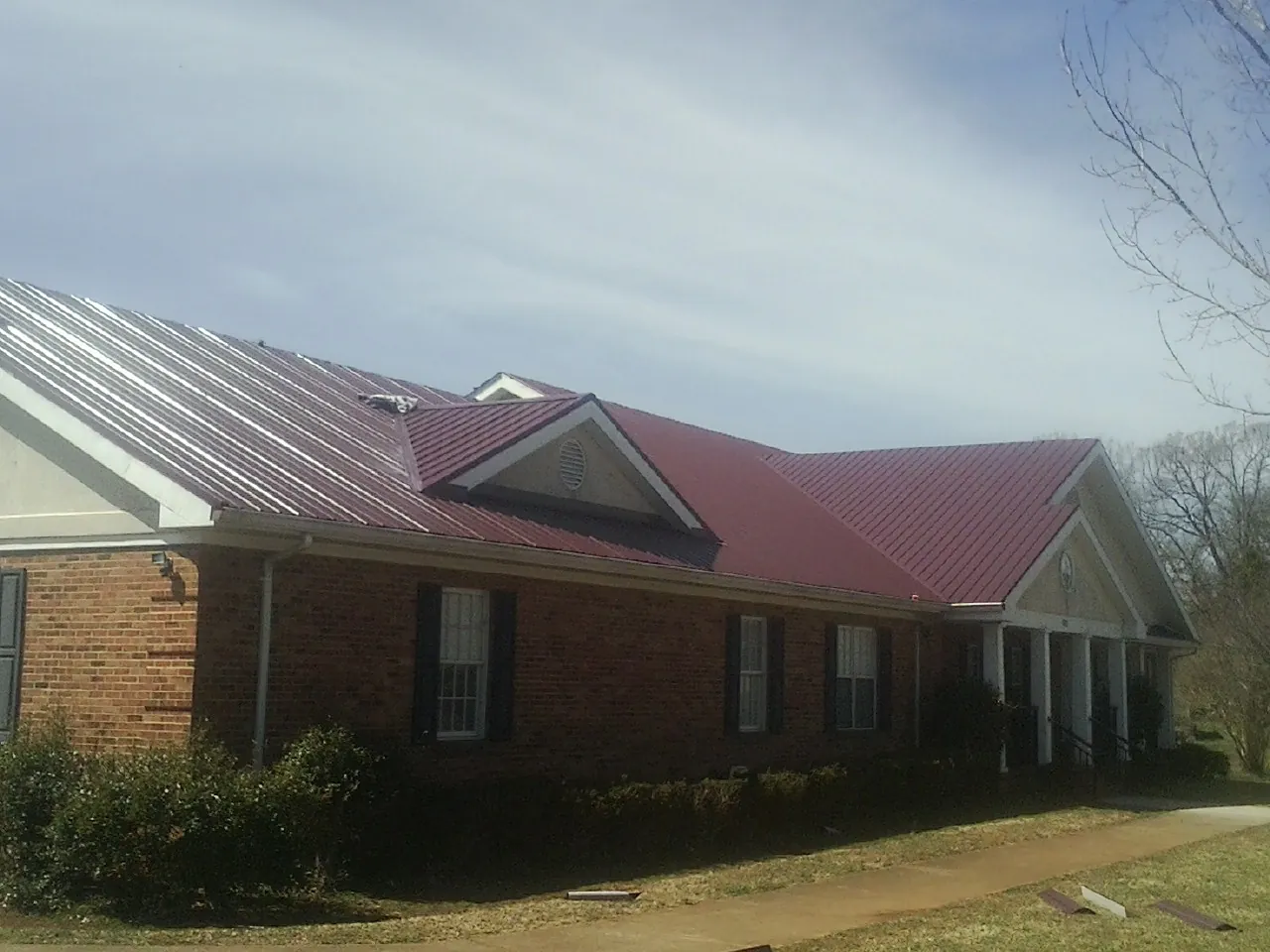 Red metal roof with gabled entries on a long brick building, from a Hail Damage Roof Repair job in Deridder
