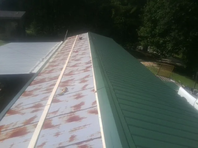 Old rusted panels beside newly installed green metal roofing — Wind Damage Roof Repair by Roofing Brothers in Deridder