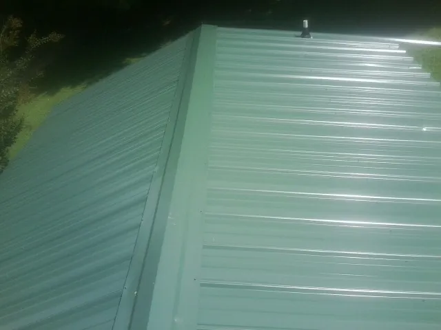 New green metal panels meeting at the ridge of a roof — Flat Roof Repair work by our crew in Deridder