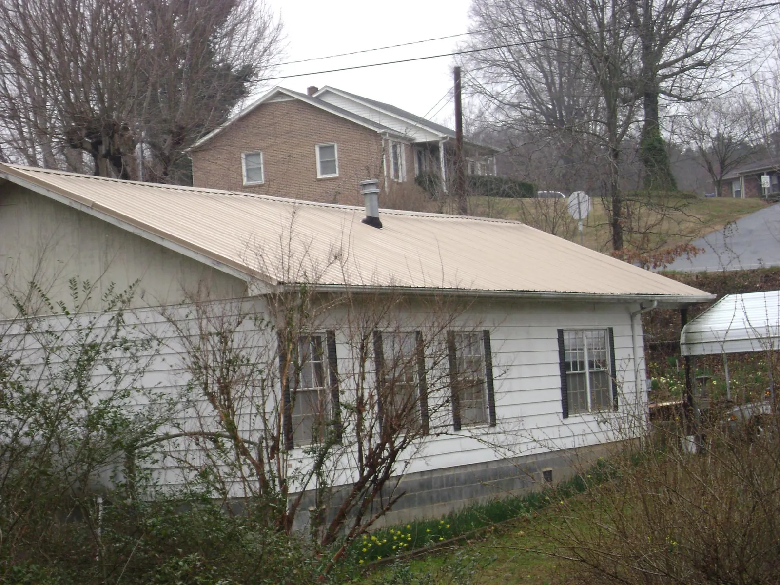 Tan metal roof on a white sided house set into a hillside — Commercial Roofing by Roofing Brothers in Deridder