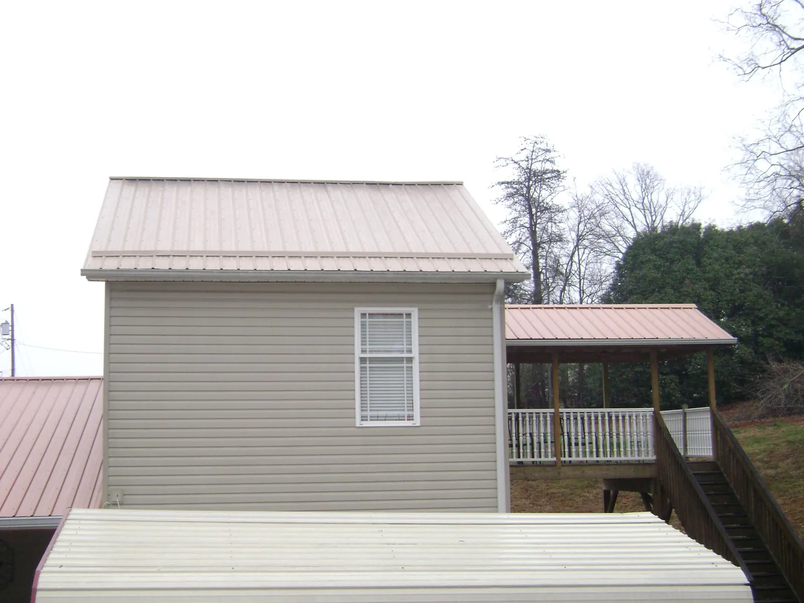 Tan metal roofs on a two story addition and attached porch, from a Roof Replacement job in Deridder